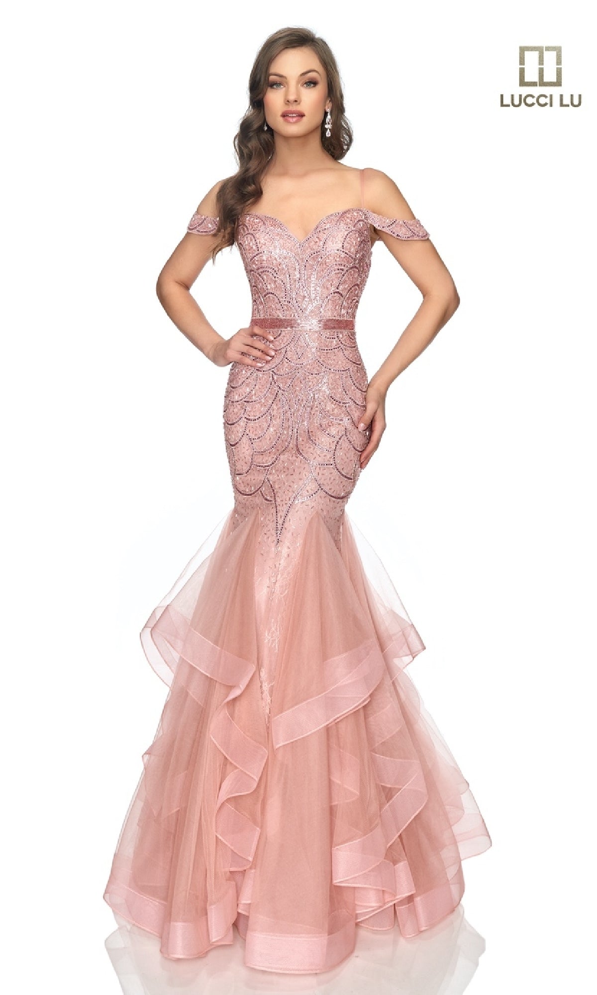 A woman stands against a white background in the Open-Back Beaded Mermaid Prom Dress: Lucci Lu 2147, featuring a pink off-the-shoulder, form-fitting silhouette with layered tulle skirt, sequin details, and beaded lace accents.
